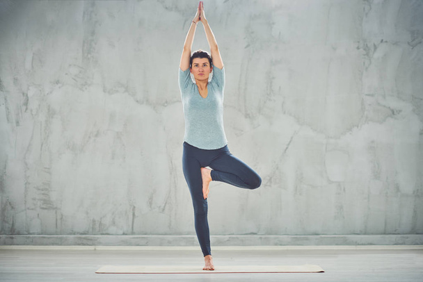 Volledige lengte van mooie Kaukasische brunette doen boom yoga pose op mat Barefoot. - Foto, afbeelding