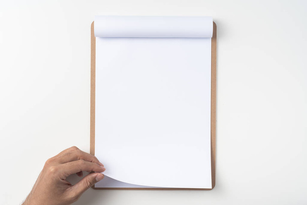 Top view of man hand holding white A4 flipped paper on brown clipboard isolated on white background - Foto, Imagen