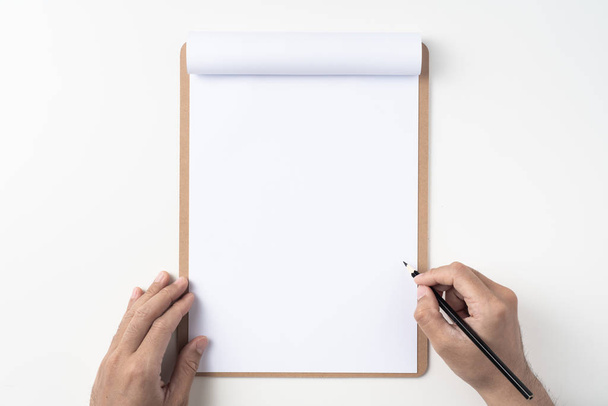 Top view of man hands holding pencil on white A4 flipped paper with brown clipboard isolated on white background. - Фото, зображення