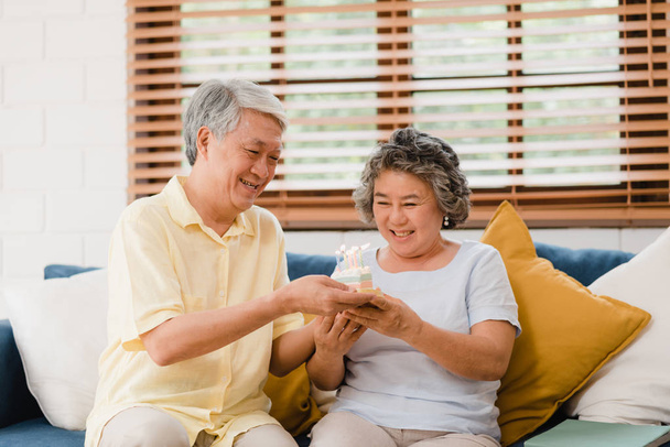 Aziatische ouderen paar man Holding cake vieren van de verjaardag van de vrouw in de woonkamer thuis. Japans koppel geniet samen thuis van liefdes moment. Lifestyle Senior Family bij Home concept. - Foto, afbeelding