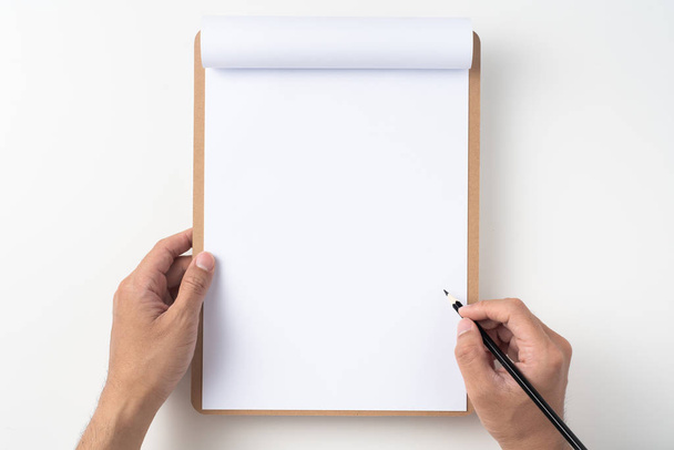 Top view of man hands holding pencil on white A4 flipped paper with brown clipboard isolated on white background. - Φωτογραφία, εικόνα