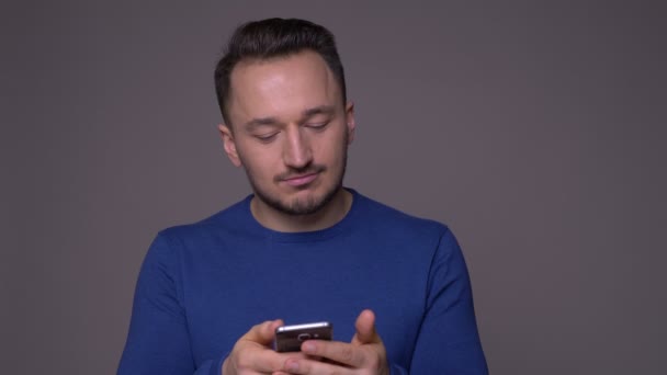 Closeup shoot of young handsome caucasian man messaging on the phone with background isolated on gray - Кадри, відео