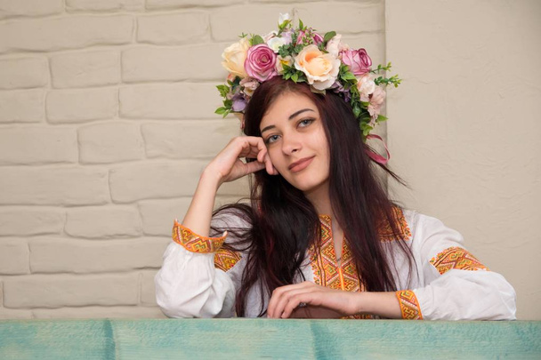 Retrato de uma menina em uma camisa bordada e com uma coroa de flores na cabeça. A grinalda é o capacete de uma rapariga ucraniana tradicional. Camisa bordada - roupa tradicional ucraniana
. - Foto, Imagem