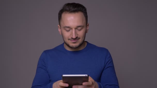 Closeup shoot of young handsome caucasian man using the tablet with background isolated on gray - Filmagem, Vídeo