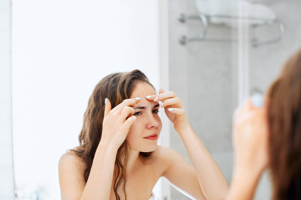 Young woman  looking and squeeze  acne on a face in front of the mirror. Ugly problem skin girl, teen girl having pimples. Skin care. Beauty - Foto, afbeelding