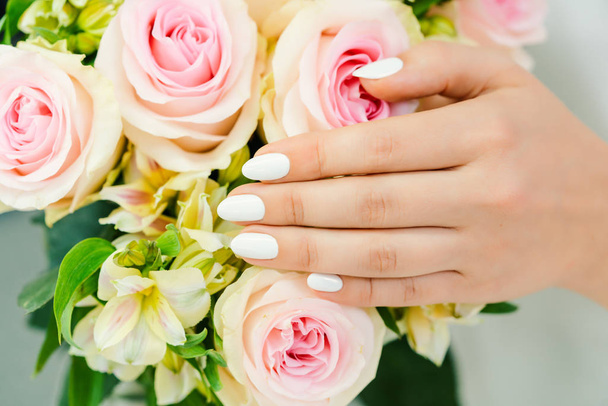 Nails of young woman with white manicure on a rose flower - Φωτογραφία, εικόνα