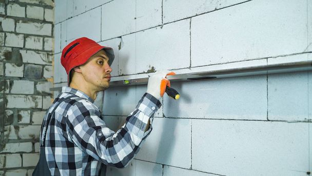 builder checking straightness of aerated concrete block wall with bubble level - Foto, Imagem