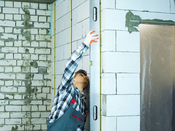 man in work wear pressing bubble level to block wall vertically - Foto, Imagem