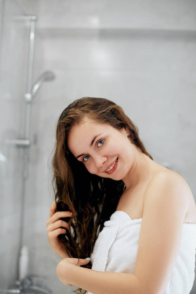 Hair And Body Care. Portrait Of Beautiful Young Female Model  in  Bath Applying Hair Oil. Closeup Of Sexy Woman In Towel Drying Wet Long Hair. Health And Beauty Concept. Protection moisturizing cream. - Fotó, kép