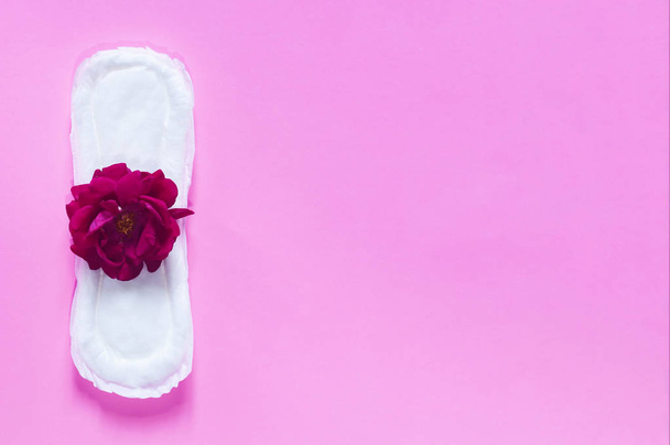 Sanitary napkin with red rose on it. On bright pink background. Period days concept showing feminine menstrual cycle. - Photo, Image