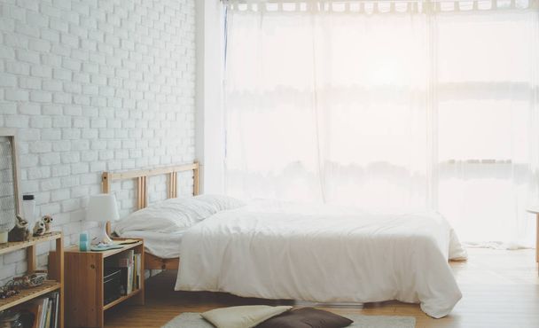 Το λευκό κρεβάτι είναι στο ηλιόλουστο υπνοδωμάτιο το πρωί. Λευκή κρεβατοκάμαρα το πρωί. Μην Εστιάστε σε αντικείμενα. - Φωτογραφία, εικόνα