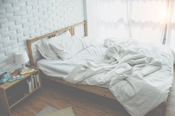 Το λευκό κρεβάτι είναι στο ηλιόλουστο υπνοδωμάτιο το πρωί. - Φωτογραφία, εικόνα
