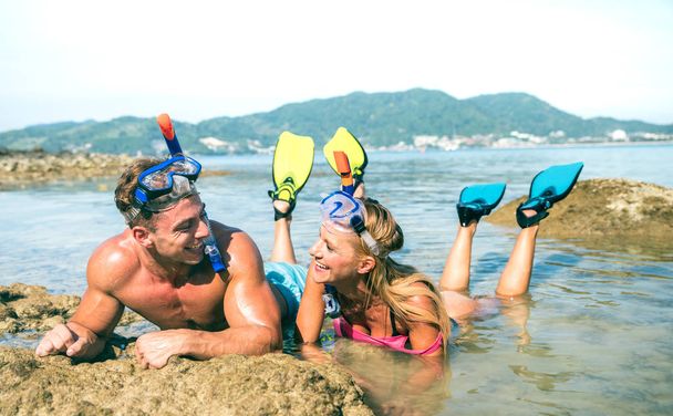 Счастливая влюбленная пара отдыхающих веселится у воды на пляже в Таиланде с маской для сноркеля и плавниками - Концепция активного молодежного путешествия по всему миру - Теплый яркий день с отфильтрованными цветовыми оттенками
 - Фото, изображение