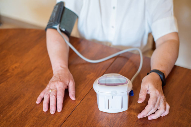 Starší žena měří krevní tlak s elektrickým zařízením. Důchodce používá tonometr. Ruce staré ženy - Fotografie, Obrázek