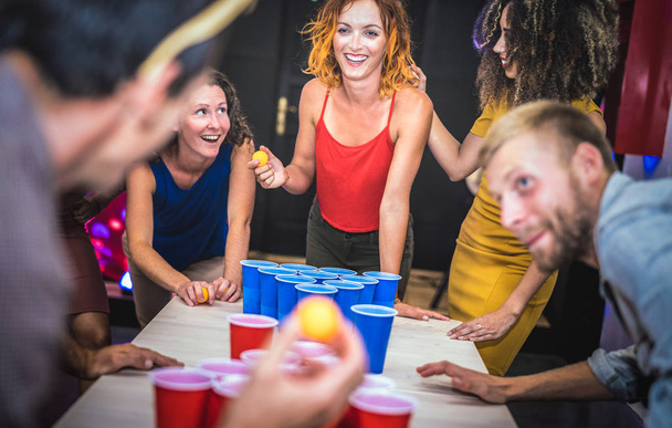 Young friends playing beer pong at youth hostel - Free time travel concept with backpackers having unplugged fun at guesthouse - Happy people on playful genuine attitude - Vivid vignetting filter - Foto, afbeelding
