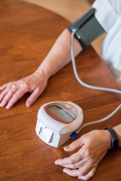 An elderly woman measures blood pressure with an electrical device. A pensioner uses a tonometer. Hands of an old woman - Zdjęcie, obraz