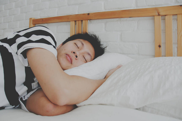 Aziatische man slapen in een witte slaapkamer. Man slaapt goed in bed in een witte slaapkamer. Ontspannen op de kamer. - Foto, afbeelding
