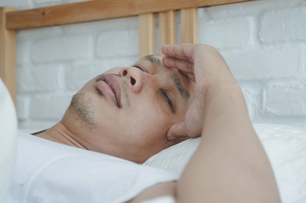 アジアの男性は、午前中に部屋の白いベッドの上に横たわって病気。寝室に男が寝ていた暖かいトーン。オブジェクトに焦点を当てない. - 写真・画像