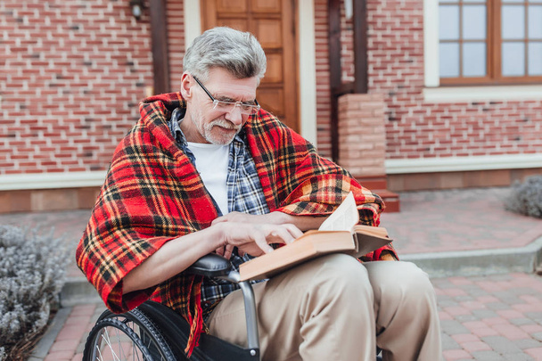 Old man on wheelchair reading interesting book  - Zdjęcie, obraz