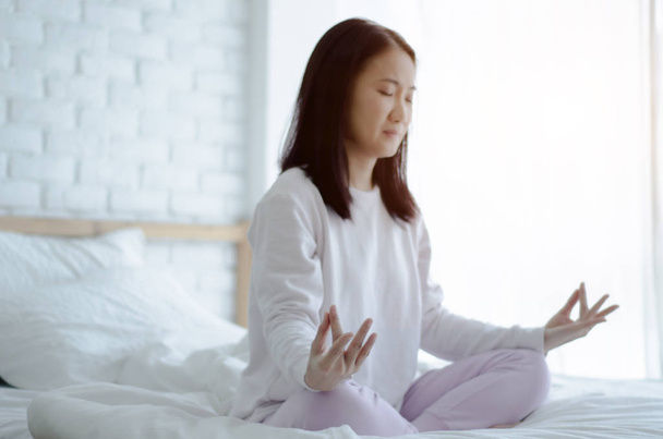 Chicas asiáticas sentadas en el yoga posa en la cama en una mañana cálida.Tonalidad cálida.No te enfoques en objetos
. - Foto, Imagen