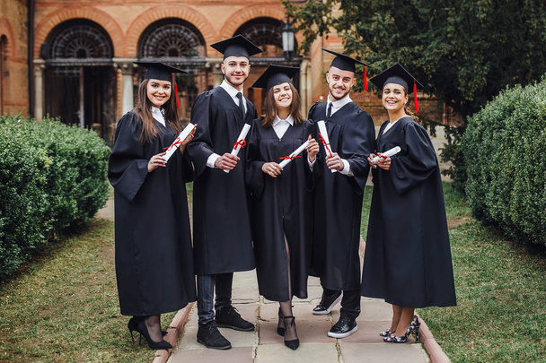 Beautiful masters with diploma in hands staying outside university - Valokuva, kuva