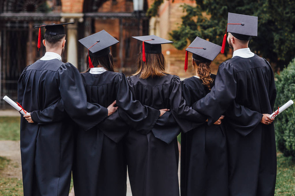Achteraanzicht van een groep van vijf studenten die diploma's aanhouden - Foto, afbeelding