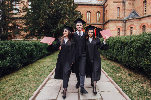 Successful graduates with diplomas walking in university garden - Zdjęcie, obraz