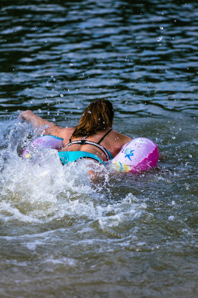 een vrouw in een lichte zwempak zwemmen weg met een water zeepbel, het creëren van een heleboel grote spatten - Foto, afbeelding