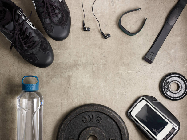 Closeup on laying on the floor black sneakers, headphones, fitness tracker, hear rate monitor, smartphone in running armband, bottle of water, weight plates. - Foto, Imagem