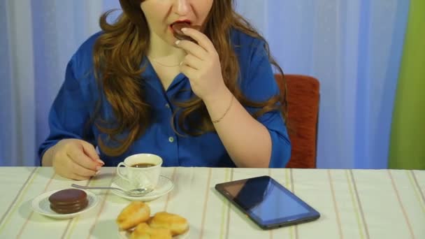 woman in a cafe at a table drinking coffee with dessert and reading the news on the tablet - Video, Çekim