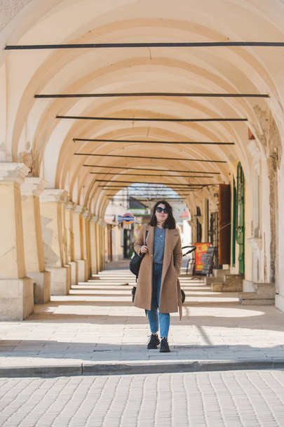 young pretty fashionable woman walking in brown coat by street - Fotoğraf, Görsel