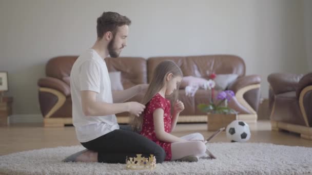 Young handsome father dressed his cute little long-haired daughters head with crown and she is happy - Filmagem, Vídeo