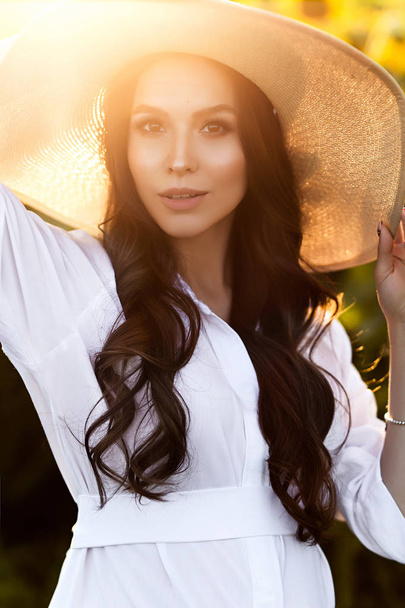 Pregnant european woman in a field of sunflowers, beautiful young european woman waiting for a child, prenant woman with dark hair in white long dress with hat on the nature - Photo, image