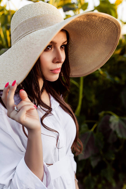 Portrait of beautiful european woman in a field of sunflowers, pretty young european woman instraw hat on nature, european woman with long dark hair in white dress with hat on the nature - Φωτογραφία, εικόνα