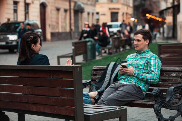 śmiech mówi mężczyzna z kobietą siedzi na ławce pitnej kawy surfowania w Internecie. miejski styl życia - Zdjęcie, obraz