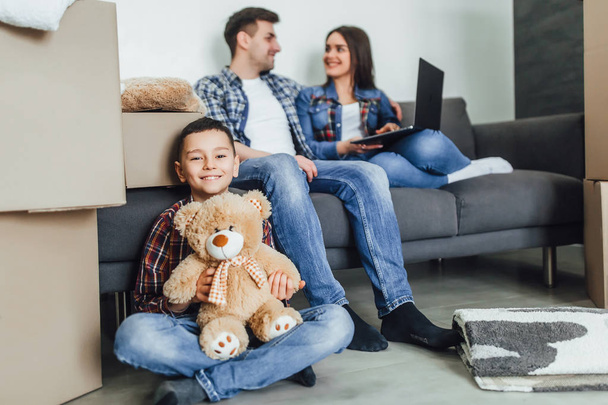 Small boy with teddy bear sitting on floor with parents using laptop  - Foto, Bild