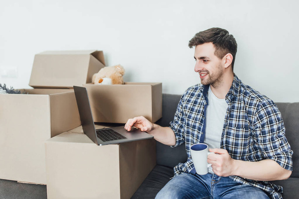 Young man using laptop on sofa with packing boxes  - Photo, image