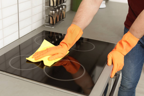 Young man cleaning oven cooktop with rag in kitchen, closeup - 写真・画像