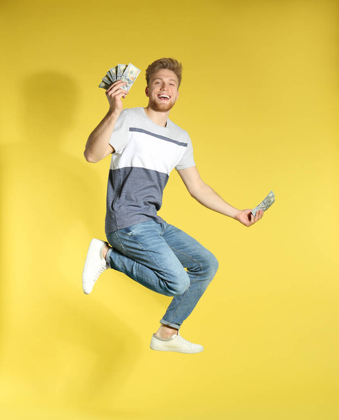 Young man jumping with money on color background - Valokuva, kuva
