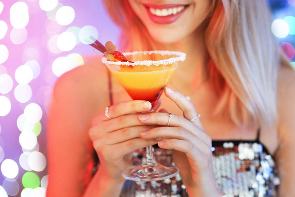 Young woman with glass of martini cocktail against festive lights, closeup - Fotografie, Obrázek