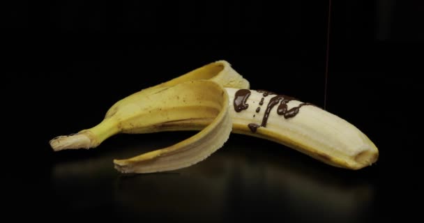 Verter un plátano con jarabe de chocolate negro derretido. Fondo negro
 - Metraje, vídeo