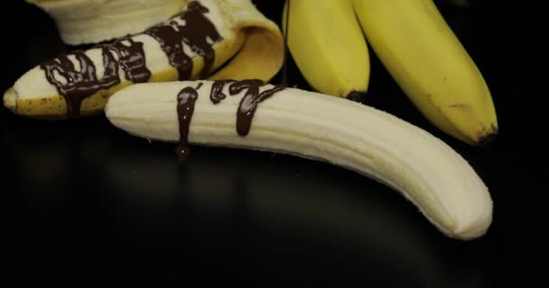 Wylewanie banana z roztopionym ciemnym syrop czekoladowy. Czarne tło - Materiał filmowy, wideo