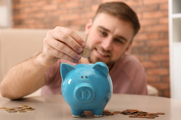 Young man with piggy bank and money at home, closeup - Foto, Imagen
