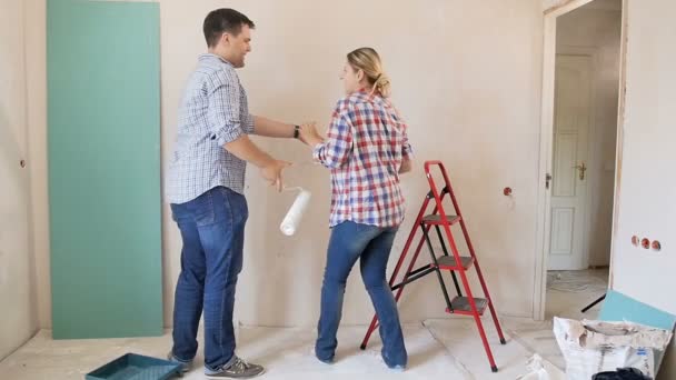Slow motion beelden van vrolijke glimlachende jonge coupledansen en springen terwijl het doen van renovatie in hun nieuwe appartement - Video