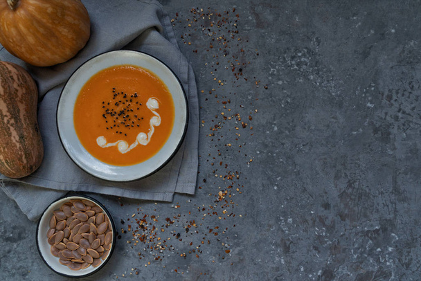 Bowl of pumpkin organic soup with cream and pumpkin seeds on gray background. Dietary vegetarian food. Concept of healthy eating food. Homemade autumn soup. Top view with copy space. Toned image. - 写真・画像