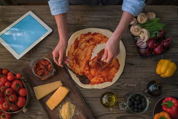Pohled shora italských potravin na tmavá rustikální stůl. Žena dělat pizzu doma pomocí digitální tabletu. Zdravé jídlo. Pojem dieta. Zdravý životní styl. Vaření doma. Připravte jídlo. Tónovaný obrázek - Fotografie, Obrázek