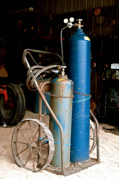 Ацетиленовый сварщик, бак газа и шланги находятся на переносной тележке с колесами в гараже
.  - Фото, изображение