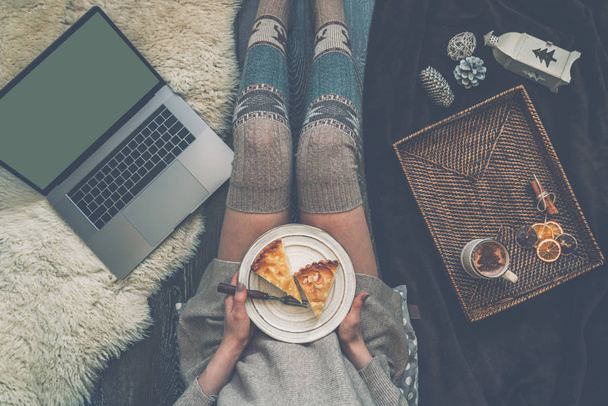 Girl holding plate of christmas cake relaxing at home, drinking cacao, using laptop. Blank screen with copy space for your text message or advertising. Warm cozy home christmas mood. Soft colors. - 写真・画像