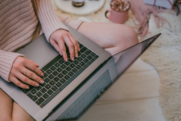 Soft cozy image. Girl in warm sweater sitting on floor near cup of coffee and cookies. Side view of a girl' hands. Woman drinking coffee in early morning and reading emails on laptop. Christmas eve. - Foto, Bild