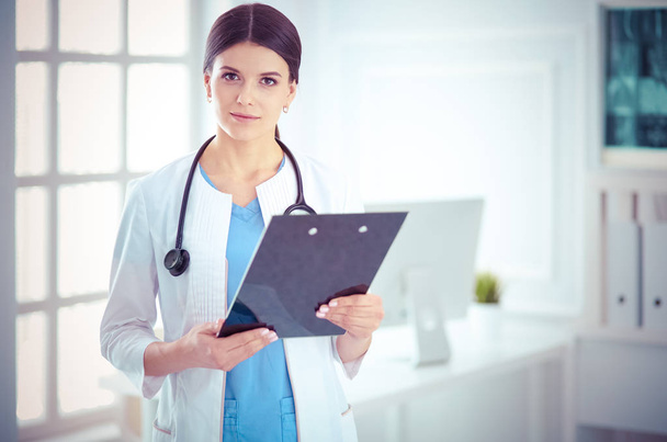 Young smiling female doctor with stethoscope holding a folder at doctors office - Foto, Bild